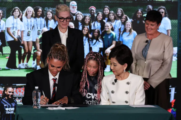 Women footballer signing professional contract reflecting salary growth in the sport